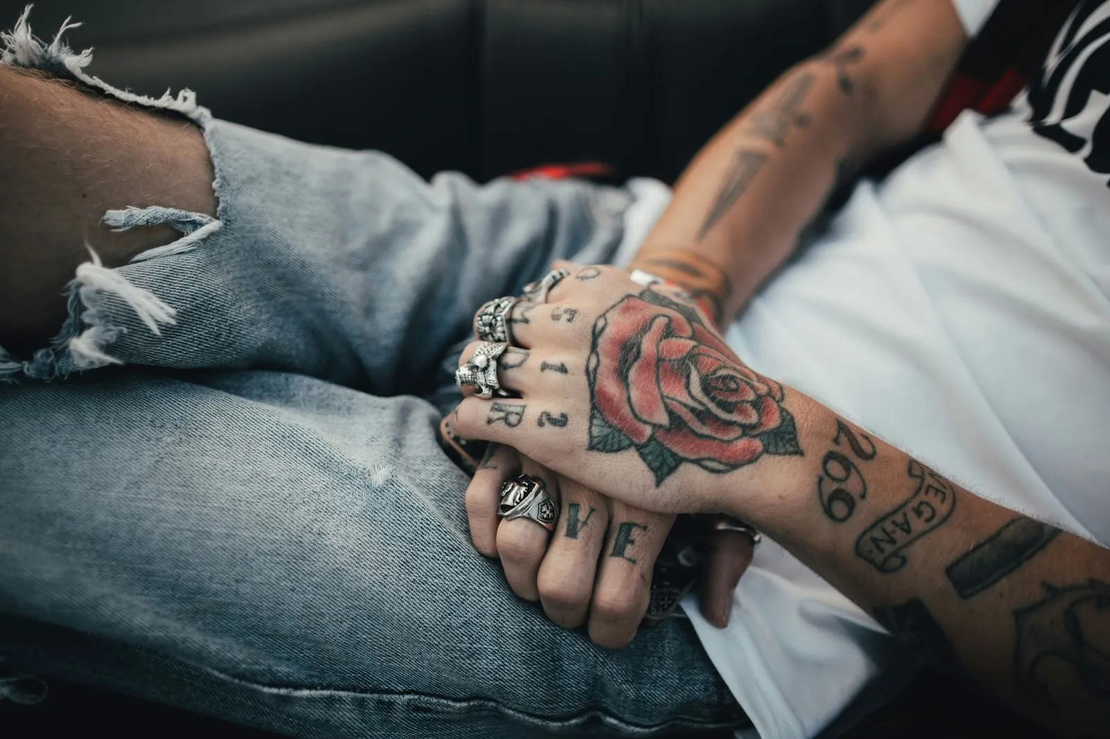 A person’s arms filled with tattoos of rose and other designs, with silvers rings worn on its fingers  