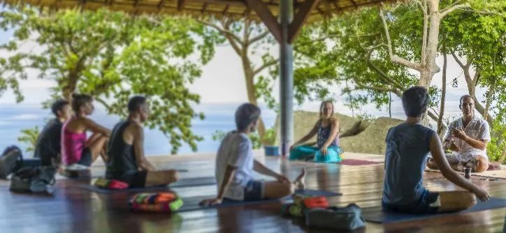 A group of people sitting comfortably on their yoga mats while listening to the instructions of their yoga teachers