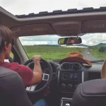 A view from the inside of a car where a couple is driving along a road with lush green grass on both sides