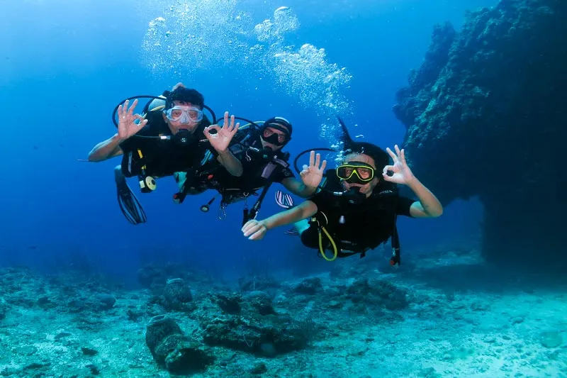 Three people making an OK sign while diving in Koh Lanta