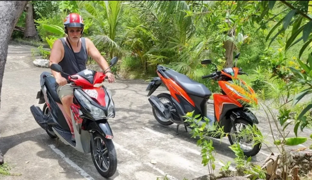 A man wearing a red helmet and riding a red and black motorbike in Koh Tao