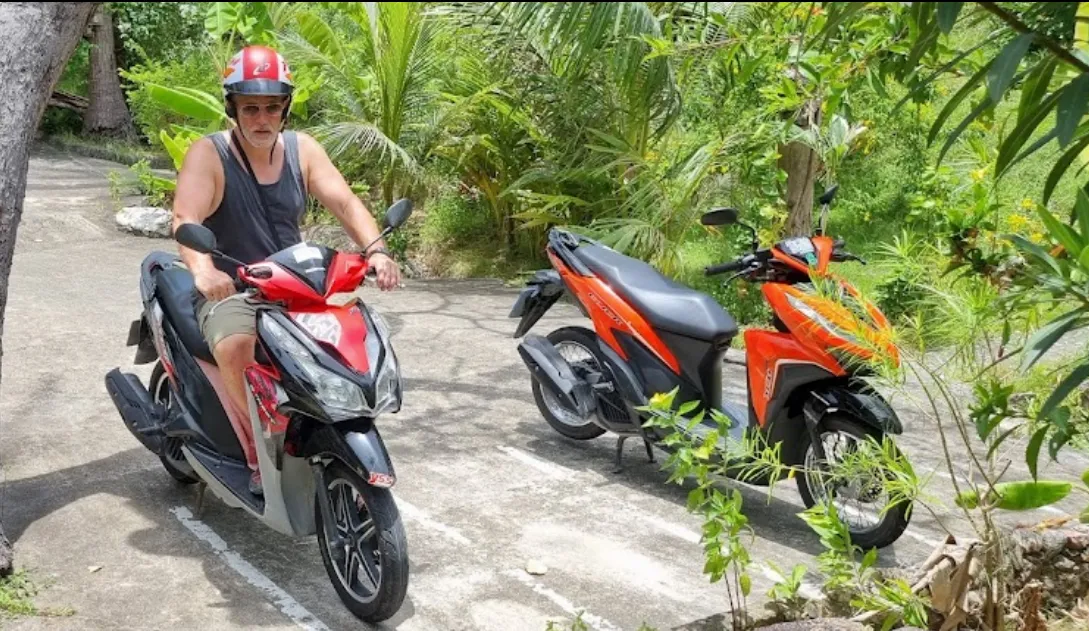 A man wearing a red helmet and riding a red and black motorbike in Koh Tao
