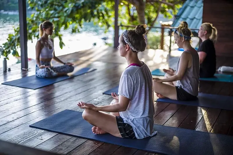 A group of three yoga students and a teacher are meditating on their yoga mats at New Heaven studio in Koh Tao

