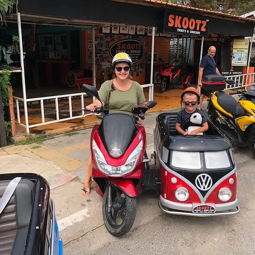 A woman and a kid riding a scooter with a sidecar outside of Skootz shop in Hua Hin