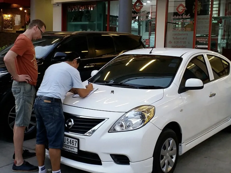 A man waiting for the staff of TN Car Rental Hua Hin to process his rented white Nissan sedan