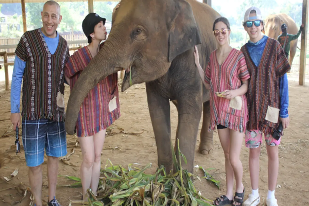 A family of visitors is enjoying the loving company of an elephant at Elephant Jungle Sanctuary in Chiang Mai
