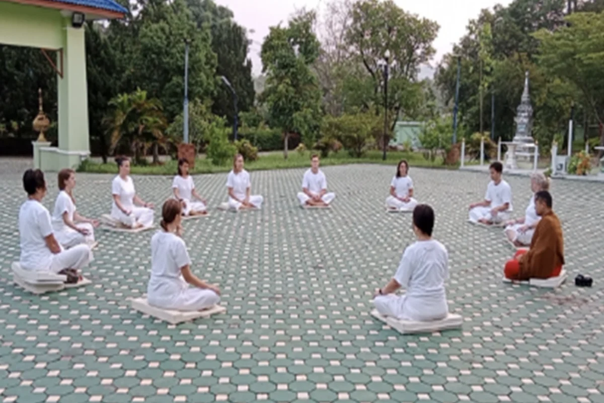 A monk and a group of students wearing white t-shirts and pants are sitting around in a circle facing each other during a meditation session at Monk Chat Retreat in Chiang Mai
