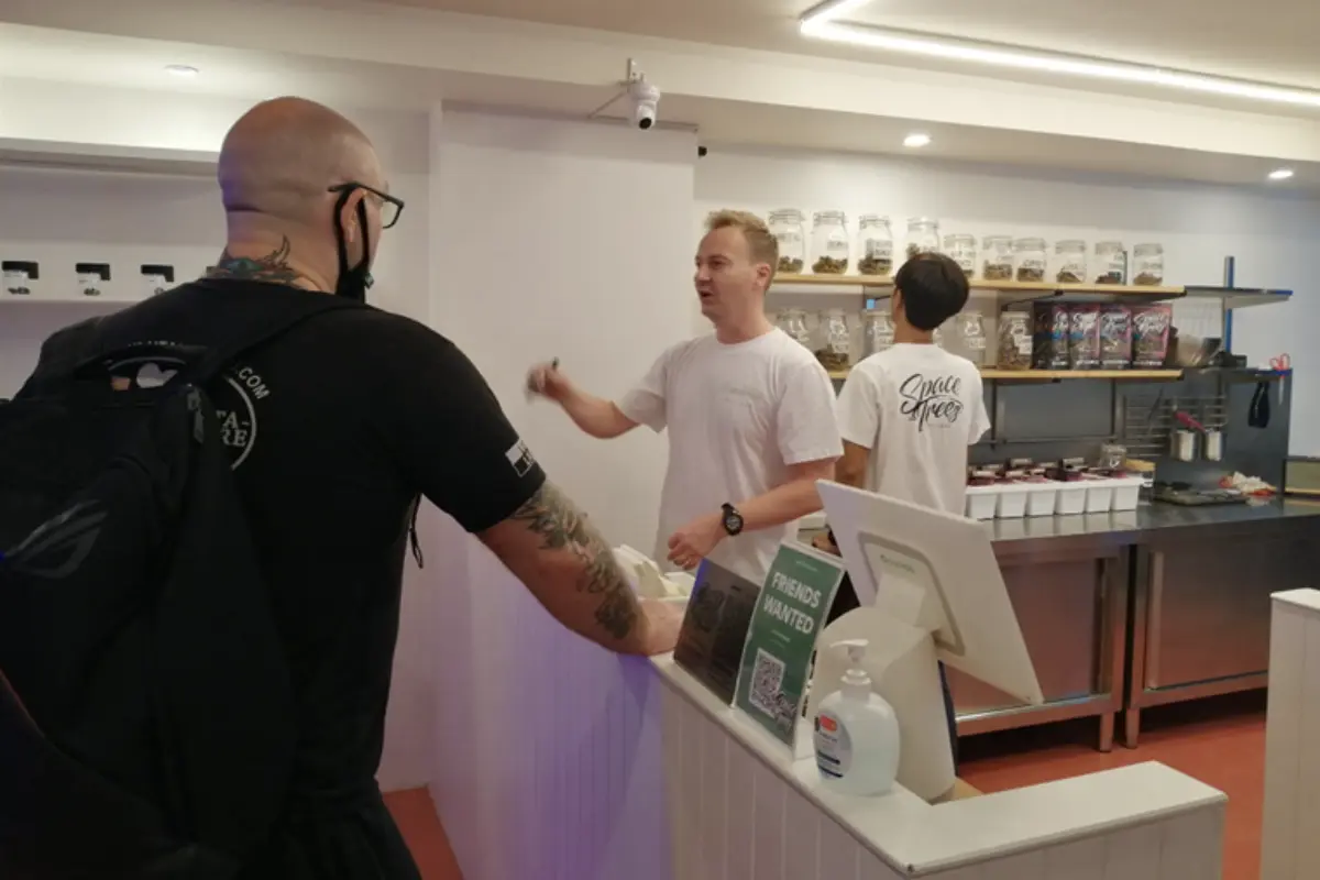 A man wearing a white t-shirt is entertaining a male customer inside Spacce Tree Cannabis Dispensary in Chiang Mai