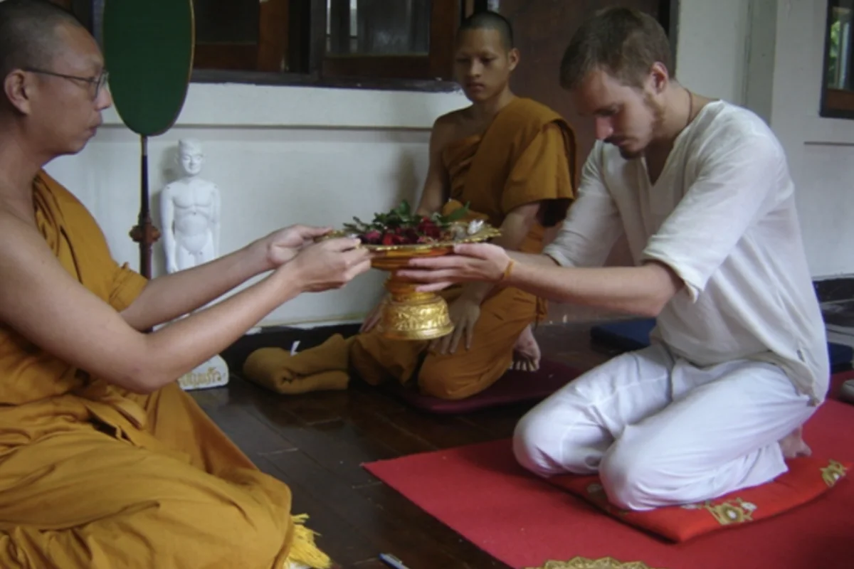 A man wearing white clothes is offering a bowl of fresh strawberry fruits to a monk during a retreat in Doi Suthep Vipassana Meditation Center in Chiang Mai