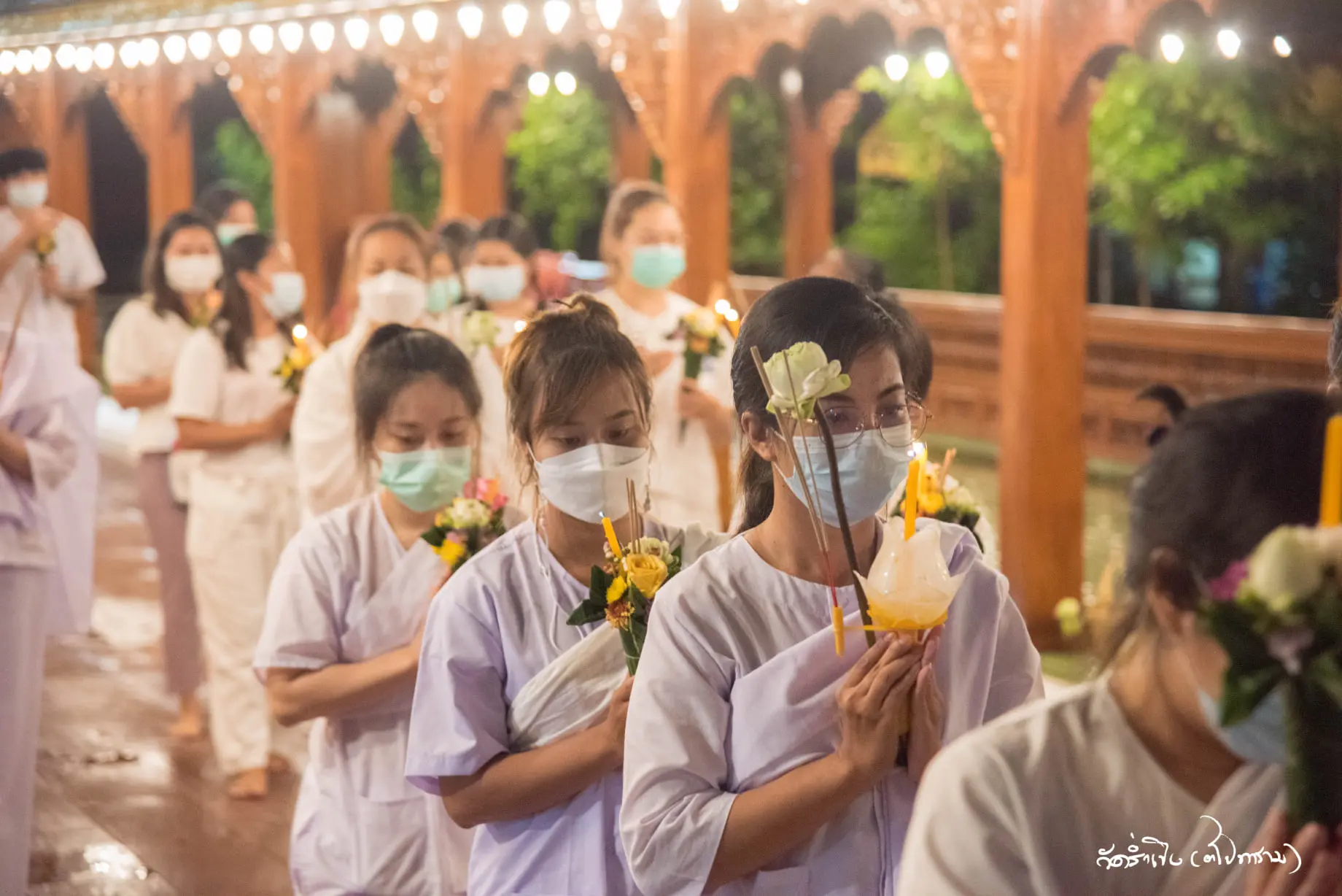 A group of women lined up in queue with prayer hands holding flowers