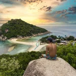 A man sitting on the edge of the cliff looking at the overview of Koh Tao