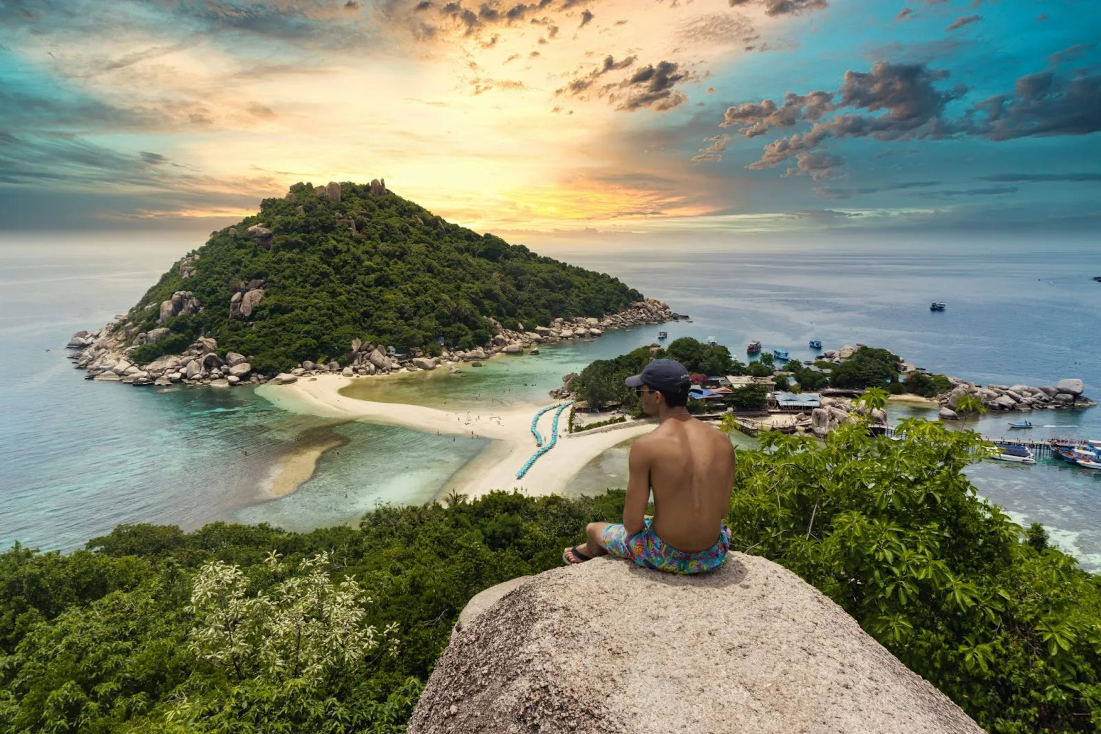 A man sitting on the edge of the cliff looking at the overview of Koh Tao