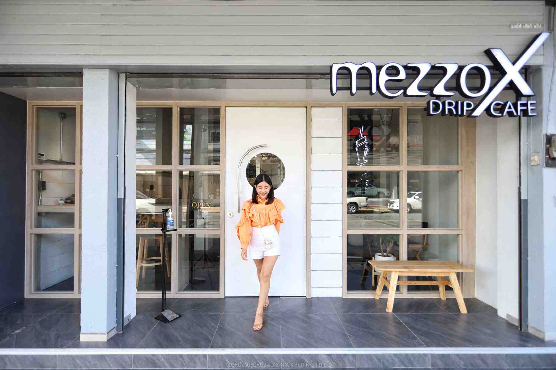 A woman wearing orange blouse and white shorts is standing in front of MezzoX Drip Cafe in Surat Thani