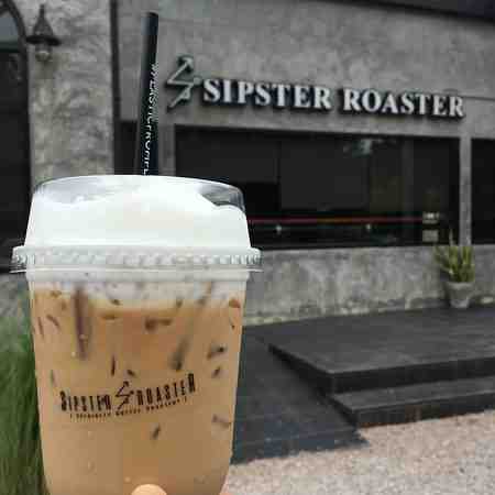 A closeup of a cup of iced coffee latte with Sipster Roaster Coffee Shop in the background 