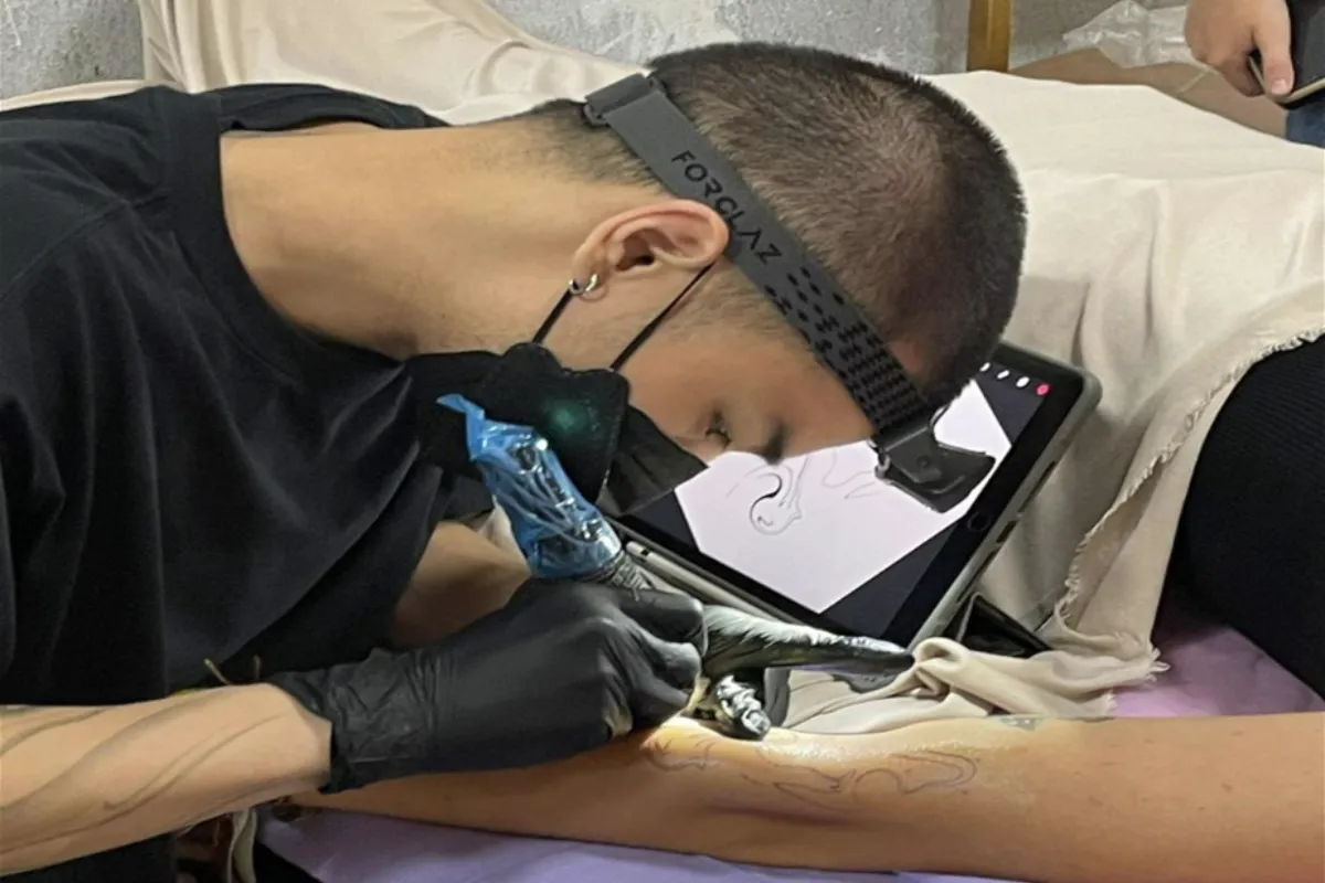 An artist is tattooing a man’s inner left upper arm at the Lee On Ink Tattoo Studio in Chiang Mai