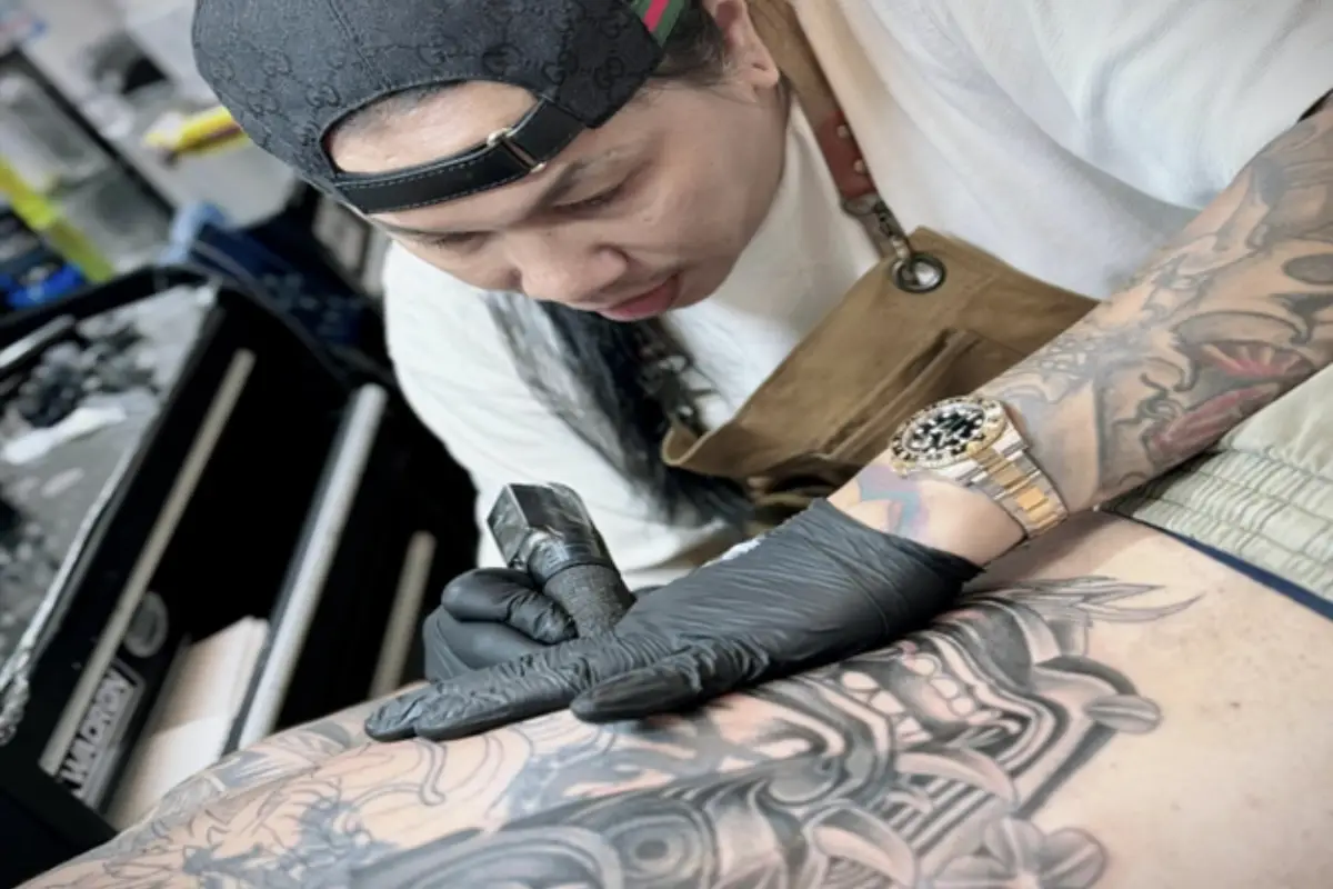 A tattoo artist is doing a tattoo of a man’s lower back at Lek Tattoo Samui in Koh Samui