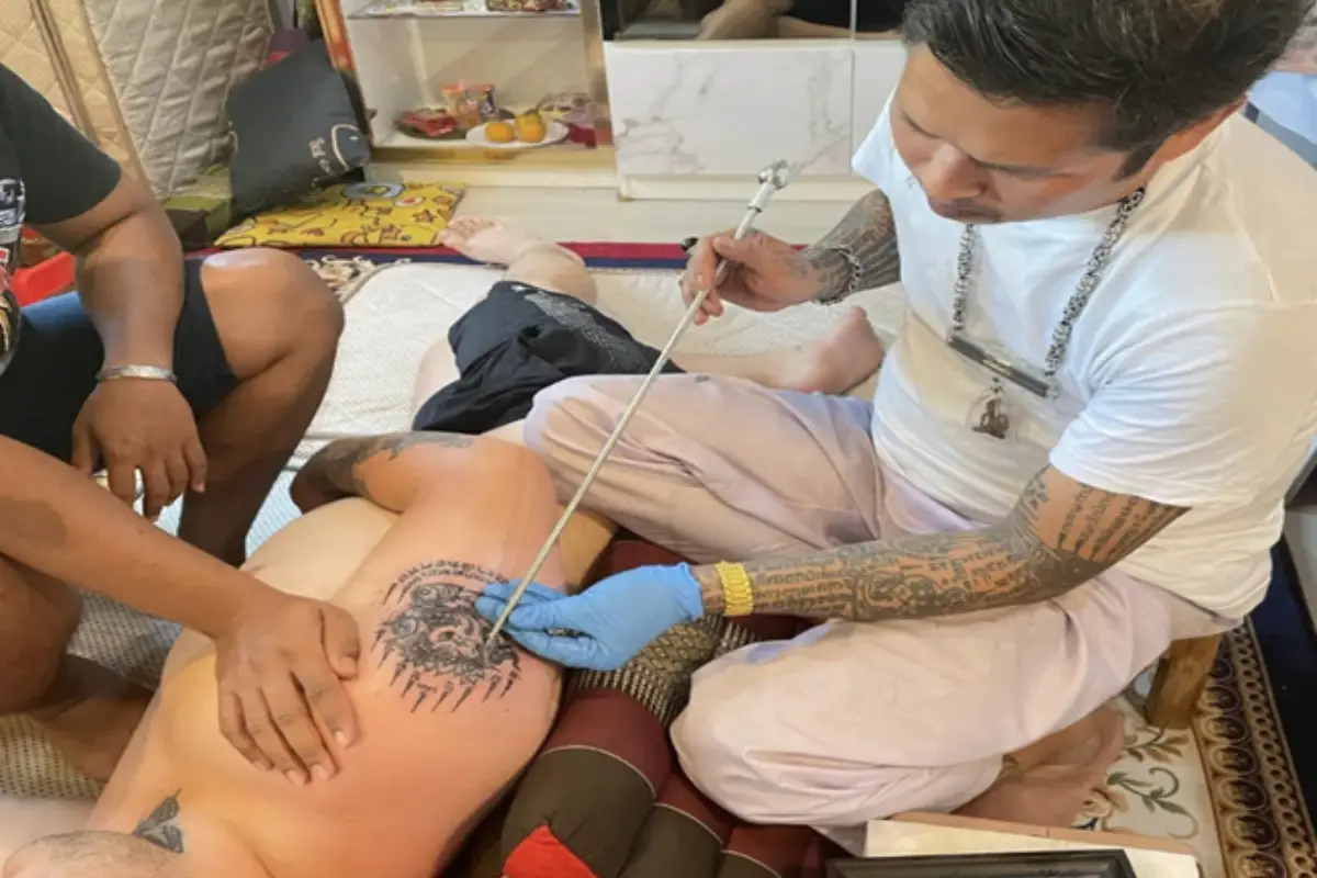 A tattoo artist is doing a sak yant tattoo on a man’s right arm at Samnak Sak Yant Ajarn Tor Choeng Moen in Koh Samui