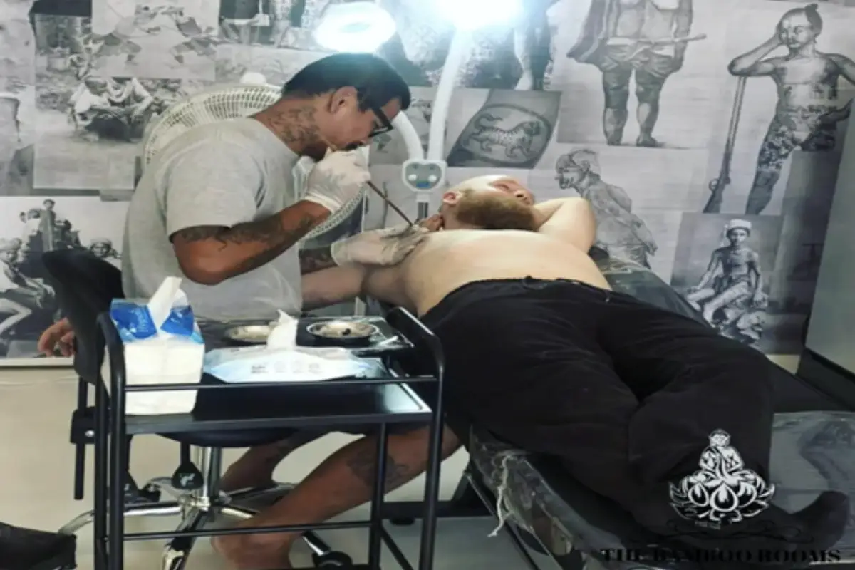 A male client is getting a hand-poked tattoo on his right chest at The Bamboo Rooms in Koh Samui