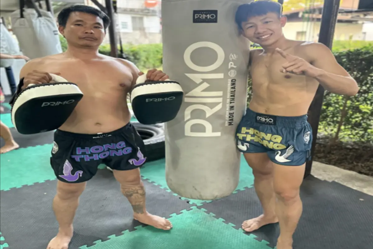 A male student and his trainer are posing for a picture beside the punching bag at Hong Thong Muay Thai Gym in Chiang Mai
