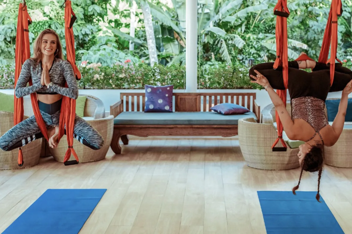 Two women hang in a yoga hammock during an aerial yoga class at Santosa Detox and Wellness Center in Phuket.