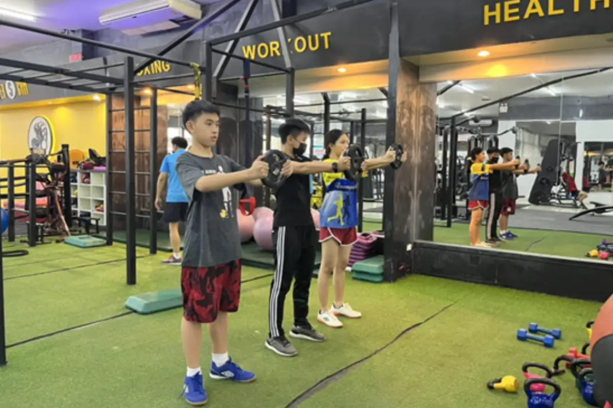 A trainer is teaching two students how to exercise with plate weights at Super Gym in Chiang Rai