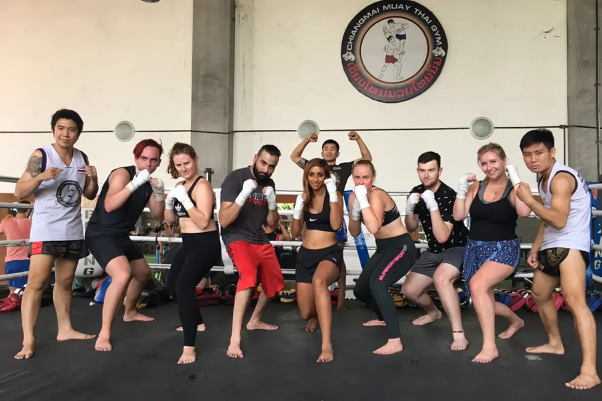 A group of men and women posing with their fighting fists on top of the ring stage of ChiangMai Muay Thai Gym