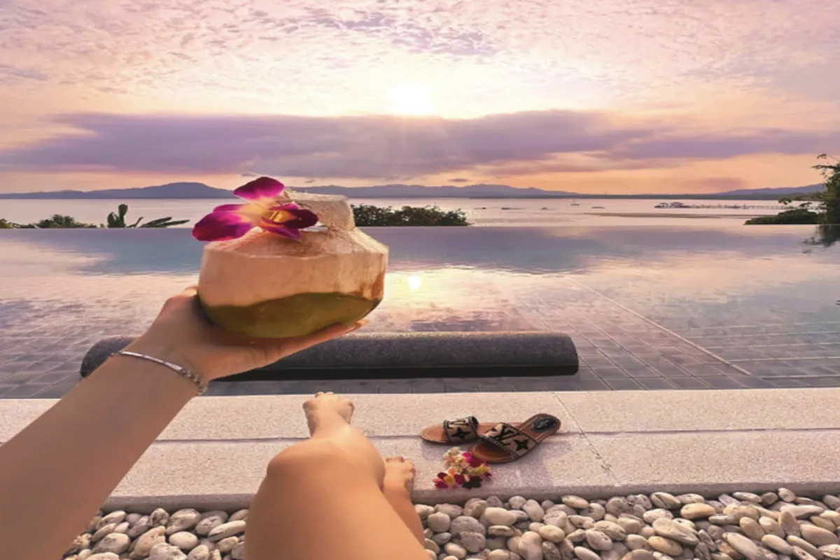 A woman’s hand holding a fresh coconut while watching the sunset across her private pool at Villa Padma resort in Phuket