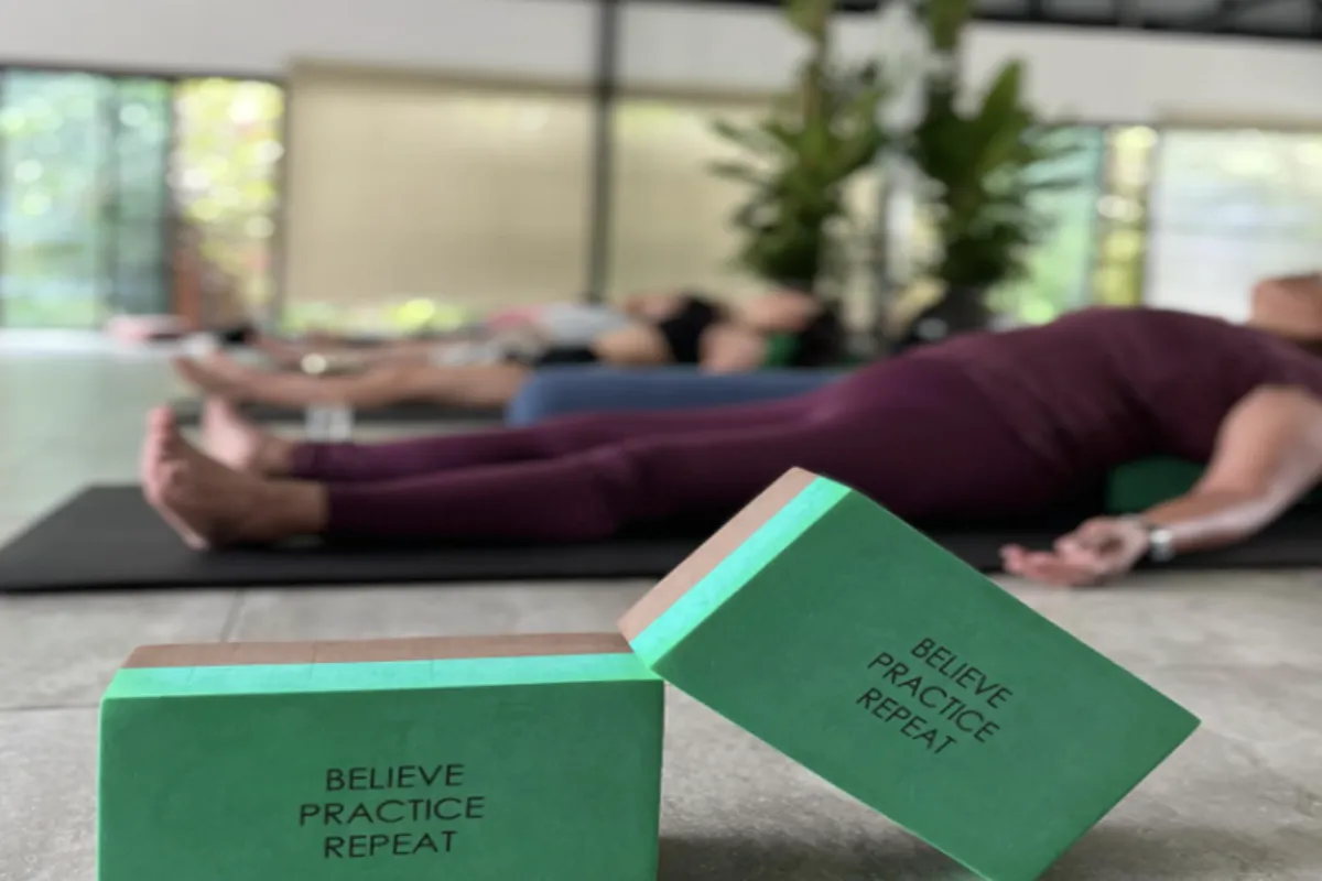 A close-up view of the yoga block with a group of people in Shavasana pose in the background.