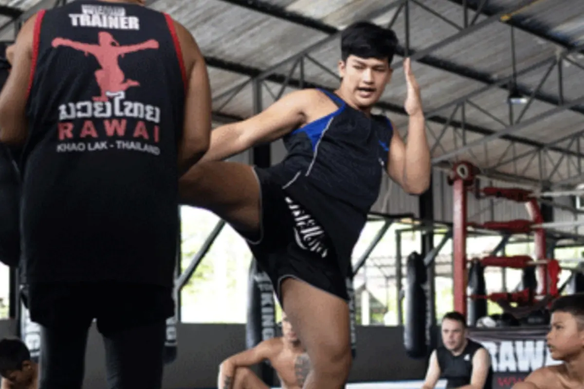 A Muay Thai trainer demonstrating a high kick in Rawai Muay Thai Gym.