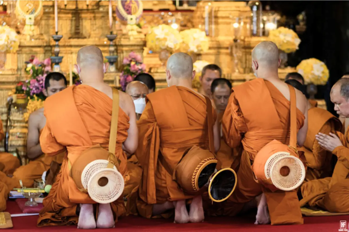 Three monks kneeling in front of other monks during their ordination ceremony at Wat Bowonniwet Vihara in Bangkok