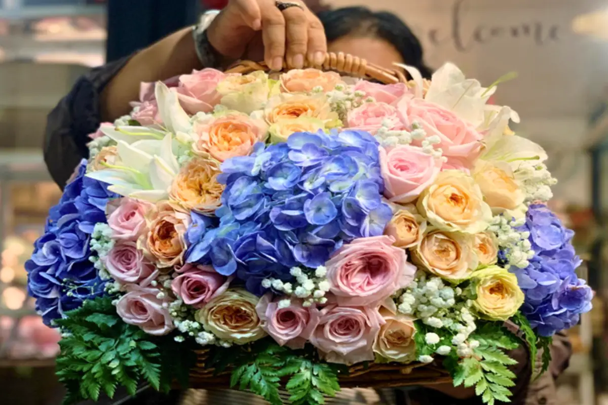 A person is holding a basket of beautifully arranged flowers created by Koset Flowers in Chiang Mai