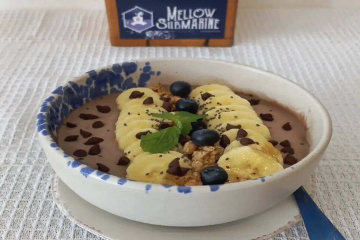 A smoothie bowl topped with slices of ripped banana, blueberries, granolas, and chocolate chips
